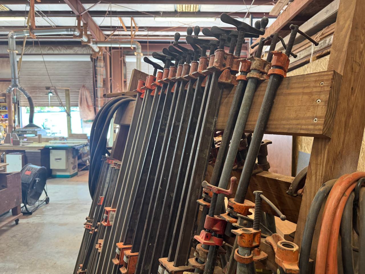 Bar clamps on a rack in the J&P Woodcrafters shop near Charleston, South Carolina — the kind used to hold a glue-up together while it dries